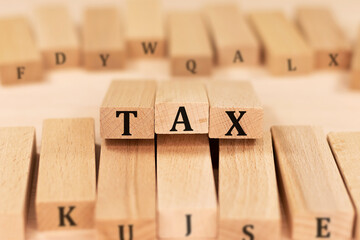 Word TAX on wooden blocks beige background top view, scattered cubes around random letters