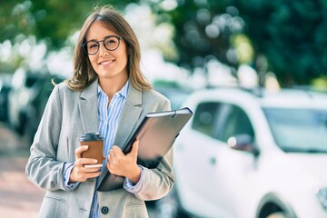 Young hispanic businesswoman drinking coffee holding binder at the city.