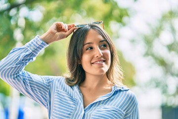 Young hispanic woman smiling happy touching her sunglasses at the park.