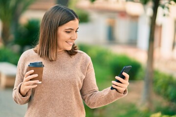 Young hispanic woman using smartphone drinking coffee at the park.