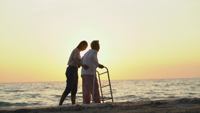 Asian senior woman use walker daughter on beautiful sunset tropical beach