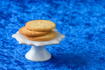 Fresh baked snowflake stamped sugar cookies on a white ceramic cake stand and blue background
