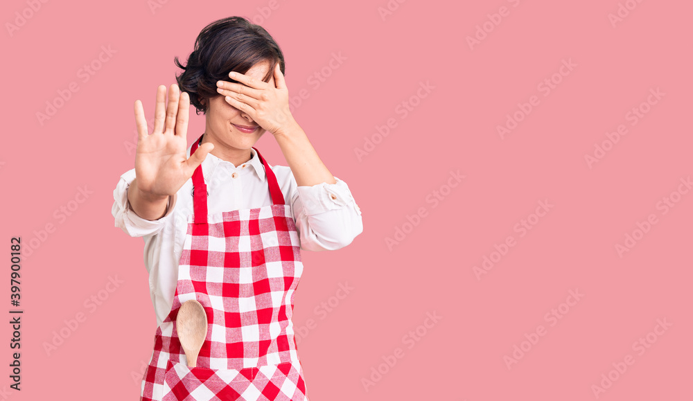 Sticker Beautiful young woman with short hair wearing professional cook apron covering eyes with hands and doing stop gesture with sad and fear expression. embarrassed and negative concept.