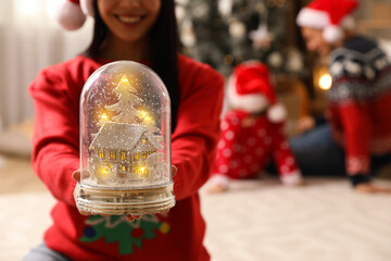Woman in red Christmas sweater holding decorative snow globe at home, closeup
