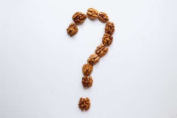Question mark made out of peeled walnuts placed on a white background