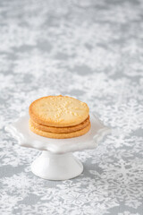 Fresh baked snowflake stamped sugar cookies on a white ceramic cake stand, and white and gray snowflake print tablecloth
