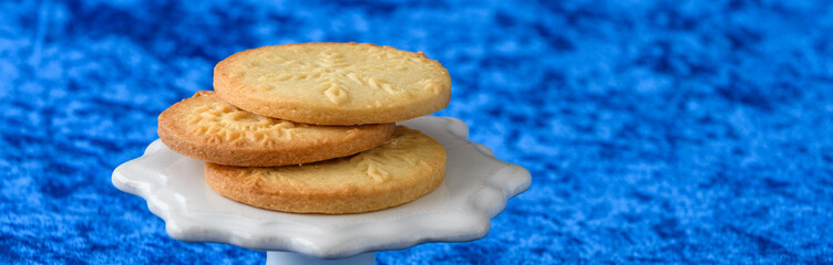 Fresh baked snowflake stamped sugar cookies on a white ceramic cake stand and blue background
