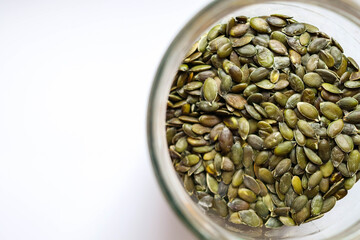 Full glass jar with peeled pumpkin seeds on white table