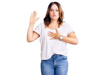 Young beautiful caucasian woman wearing casual white tshirt swearing with hand on chest and open...