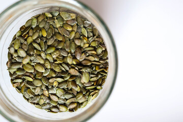 Full glass jar with peeled pumpkin seeds on white table