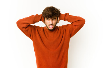 Young arab man on white background covering ears with hands trying not to hear too loud sound.