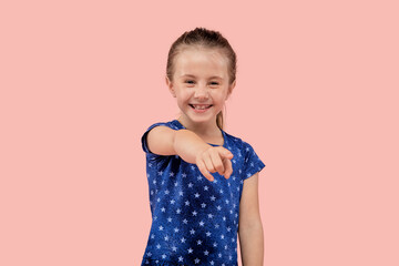 A brunette girl points her finger at the camera. In a blue dress with a small star print. Pink isolated background.