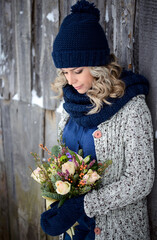 A beautiful woman holds a bouquet of roses and fir branches against a wooden wall. Stylish winter clothing