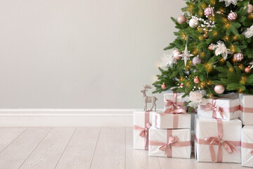 Beautiful decorated Christmas tree and gifts near light wall. Space for text