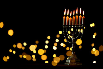 Golden menorah with burning candles against dark background and blurred festive lights, space for text