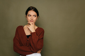 Obraz premium Young short-haired brunette woman. Thinking looking at the left side copy space, supporting her chin with her hand.