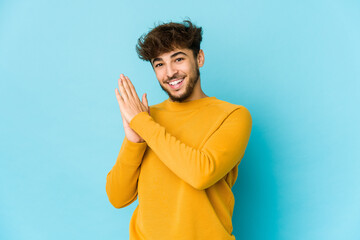 Young arab man on blue background feeling energetic and comfortable, rubbing hands confident.