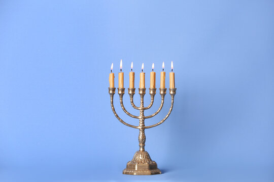 Golden menorah with burning candles on light blue background, space for text