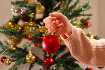 A Swedish girl holding a red Christmas ball in front of a Christmas tree. Stockholm, Sweden.