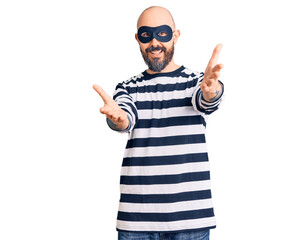 Young handsome man wearing burglar mask looking at the camera smiling with open arms for hug. cheerful expression embracing happiness.