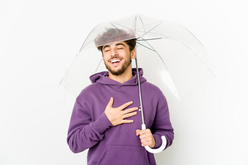 Young arab man holding an umbrella laughs out loudly keeping hand on chest.