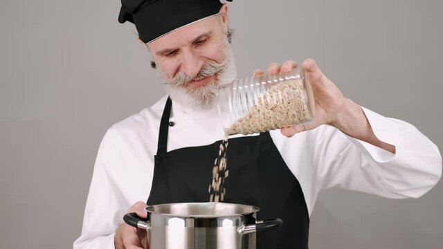 Cooking, healthy food. Professions and jobs. The man in chef's equipment standing with a pot and bootle of cereals on grey copy space.