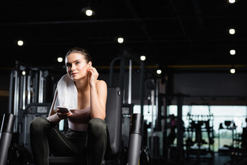 Fototapeta na wymiar smiling sportswoman listening music in wireless earphone while holding smartphone in gym