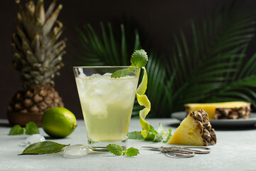 Refreshing,tropical Pineapple cocktail or detox juice in a glass with ice,mint leaves and lime in a front of palm leaves.Close up of pineapple cocktail.