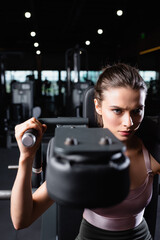 Fototapeta na wymiar sportive woman doing arms extension exercise on training machine on blurred foreground