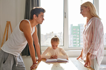 parents of child arguing while he is studying at home, sitting with book at table, they have...