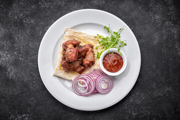 Fried shish kebab with lavash, sauce, microgreen and onion, on a white plate, on a gray background. top view