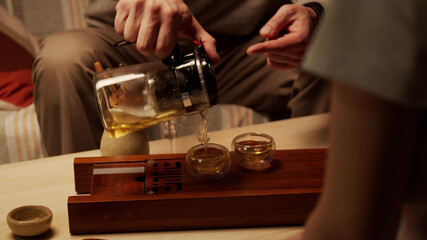 Close up. An asian tea ceremony master teaches a student the mystery of brewing chinese herbal tea in a teapot.
