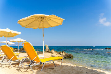 Rows of yellow beach umbrellas and sun beds on the white sand close to the crystal clear waster of Mediterranean sea. Ideal 5 star blue flag beach in Greece, Halkidiki. Tourist paradise. 