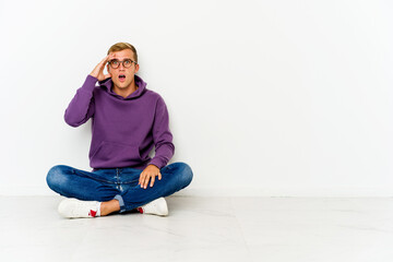Young caucasian man sitting on the floor shouts loud, keeps eyes opened and hands tense.