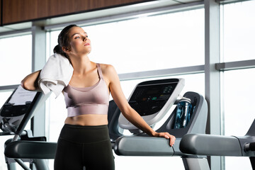 Fototapeta premium young sportswoman wiping neck with towel while standing on treadmill