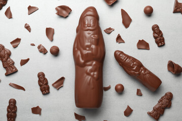 Flat lay composition with whole and broken chocolate Santa Claus candies on light grey table