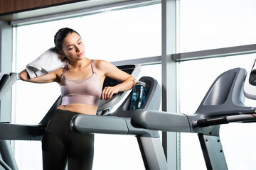 Fototapeta na wymiar sportswoman in bra and leggings wiping neck with towel while standing on treadmill