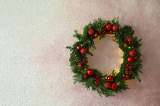 Beautiful Christmas Wreath With Festive Decor On Light Pink Wall, Space For Text