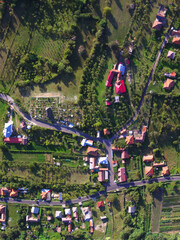 Aerial top view of a rural village in Romania. An road intersection, the church and the surrounding hill can be seen in this image.