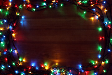 Frame of colorful Christmas lights on wooden table, top view. Space for text