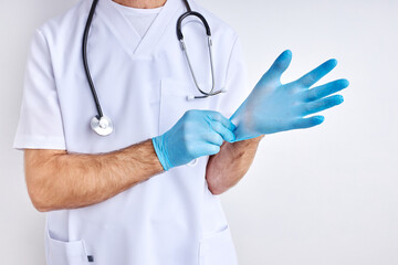 cropped male doctor is wearing gloves preparing for work, wearing white robe, isolated in studio with white background