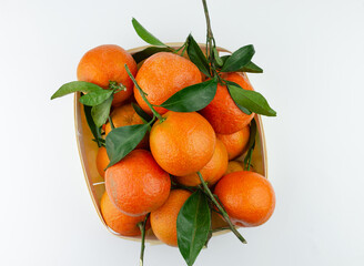 Extra sweet and juicy Spanish clementines with leaves in a basket. Isolated on white. Top down view.