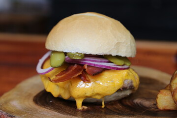 Hamburger. Made on the barbecue grill. With cheese, bacon, onion, pickle. On wooden background