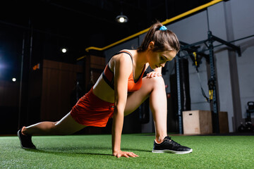 athletic sportswoman doing forward lunges exercise while warming up in gym