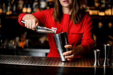 woman bartender holds scoop and accurate pours ice cubes into shaker glass