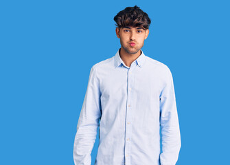 Young hispanic man wearing casual shirt puffing cheeks with funny face. mouth inflated with air,...