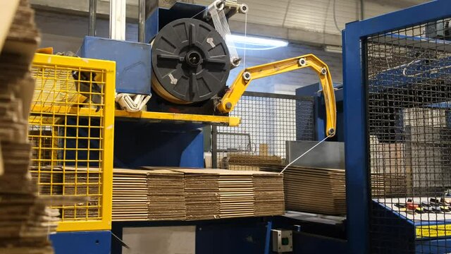 Ready-made cardboard boxes are moved in stacks along an automated packaging line. The strapping machine packs the stacks with thick white thread.  Paper corrugated box factory.