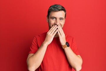 Handsome caucasian man wearing casual red tshirt laughing and embarrassed giggle covering mouth...
