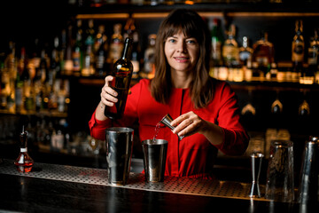 woman bartender accurate pours liquid from jigger into steel shaker cup standing on bar