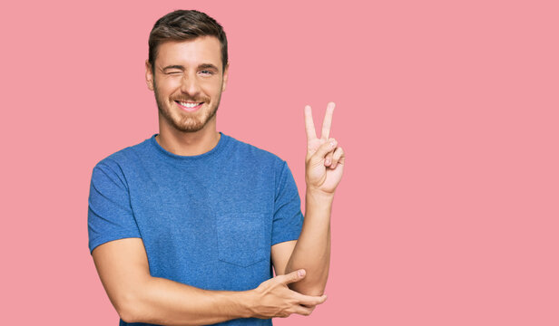 Handsome caucasian man wearing casual clothes smiling with happy face winking at the camera doing victory sign. number two.